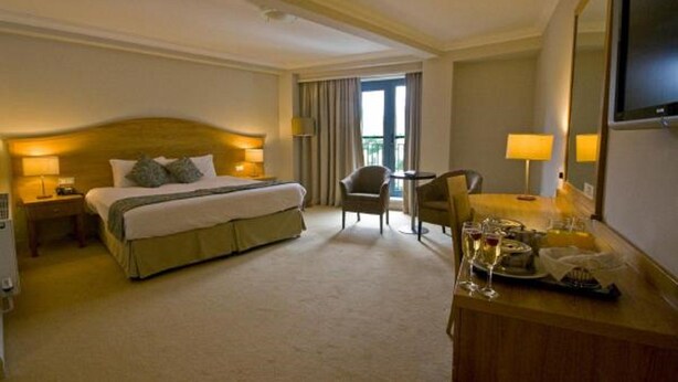 Habitación de hotel con una cama grande, un escritorio con silla, televisión y ventana con cortinas.