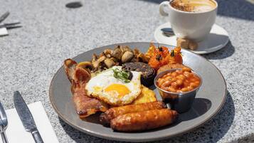 A plate of breakfast food including eggs, sausages, beans, and toast, with a cup of coffee on the side.