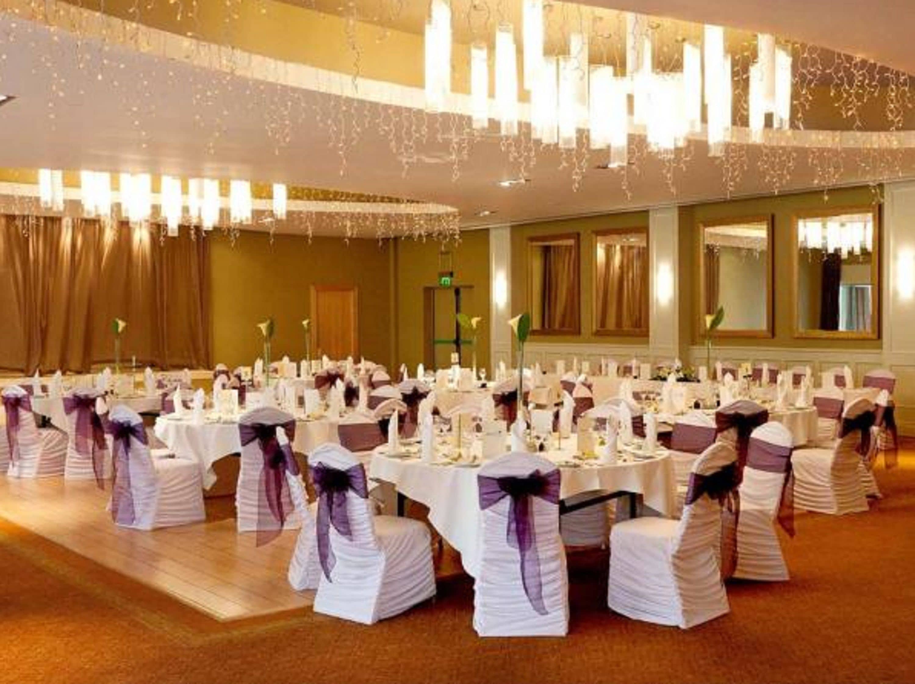 A banquet hall with round tables, white tablecloths, and chairs with purple sashes.