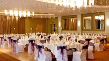 A banquet hall with round tables, white tablecloths, and chairs with purple sashes.
