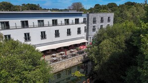 Un edificio de varios pisos con asientos al aire libre y un puente de piedra sobre una fuente de agua reflectante.