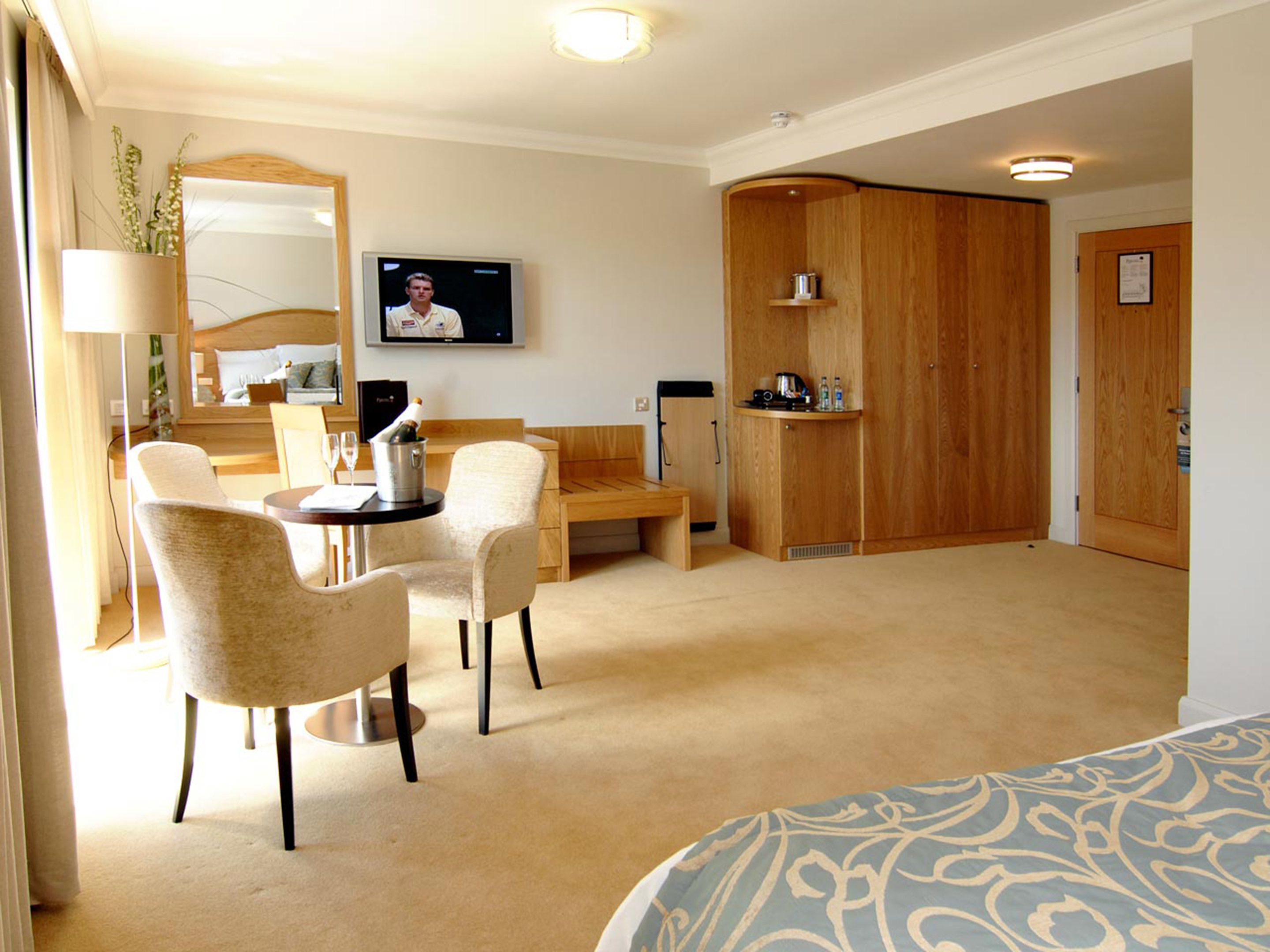 Habitación de hotel con cama, escritorio, dos sillas, televisor, armario de madera y pequeña cocina.