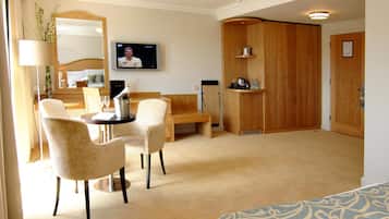 A hotel room with a bed, a desk, two chairs, a television, a wooden wardrobe, and a small kitchenette.