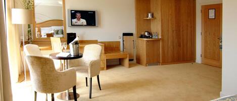 Habitación de hotel con cama, escritorio, dos sillas, televisor, armario de madera y pequeña cocina.