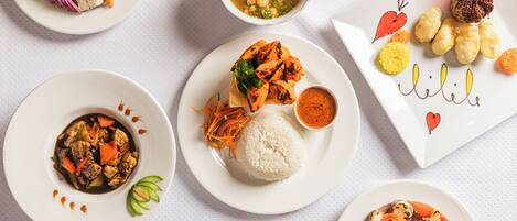 A variety of dishes on white plates, including grilled chicken, rice, and vegetables.