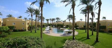 A resort with a central pool, palm trees, and well-maintained lawns.