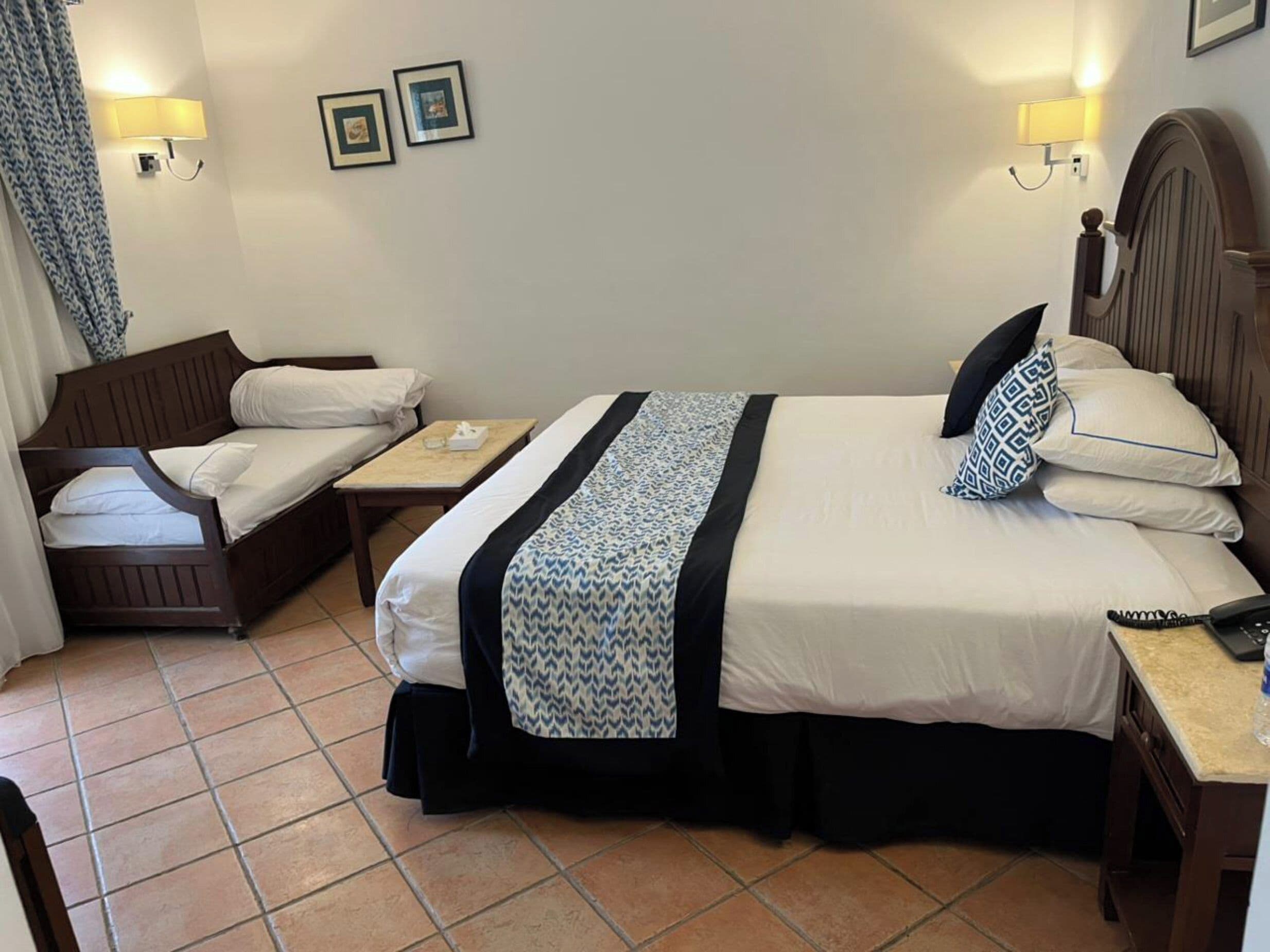 Habitación de hotel con dos camas, una mesita y dos lámparas fijadas a la pared.