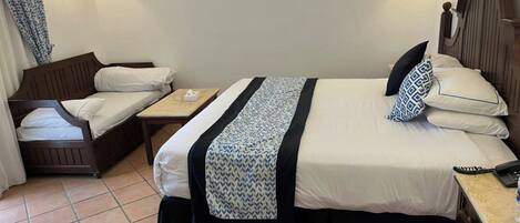 Habitación de hotel con dos camas, una mesita y dos lámparas fijadas a la pared.