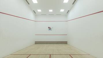 A squash court with a wooden floor, white walls, and red lines marking the boundaries.