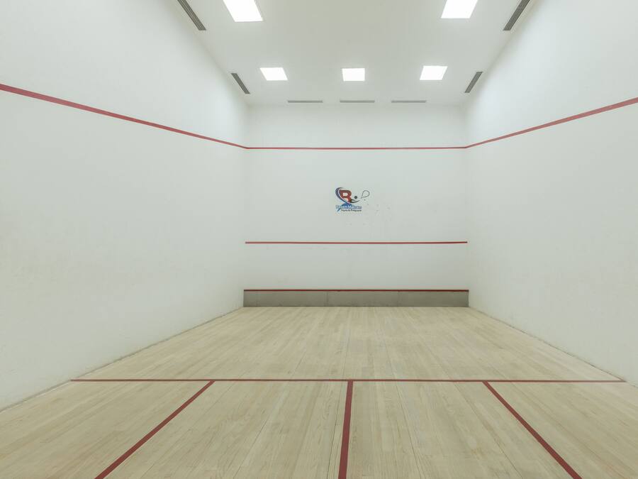 A squash court with a wooden floor, white walls, and red lines marking the boundaries.