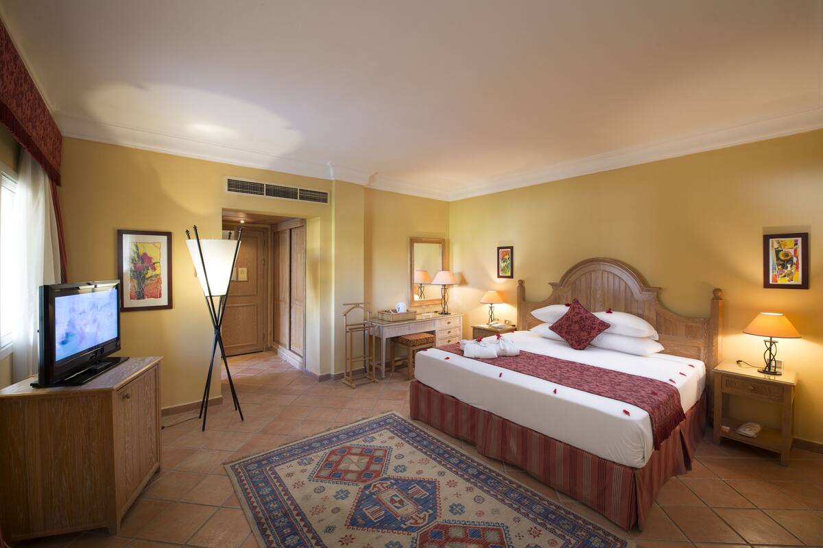 Une chambre d’hôtel comprenant un lit, des lampes de chevet, un bureau, une télévision et un grand tapis.