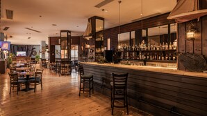 Zona de bar con suelo de madera, taburetes y una variedad de botellas en estanterías.