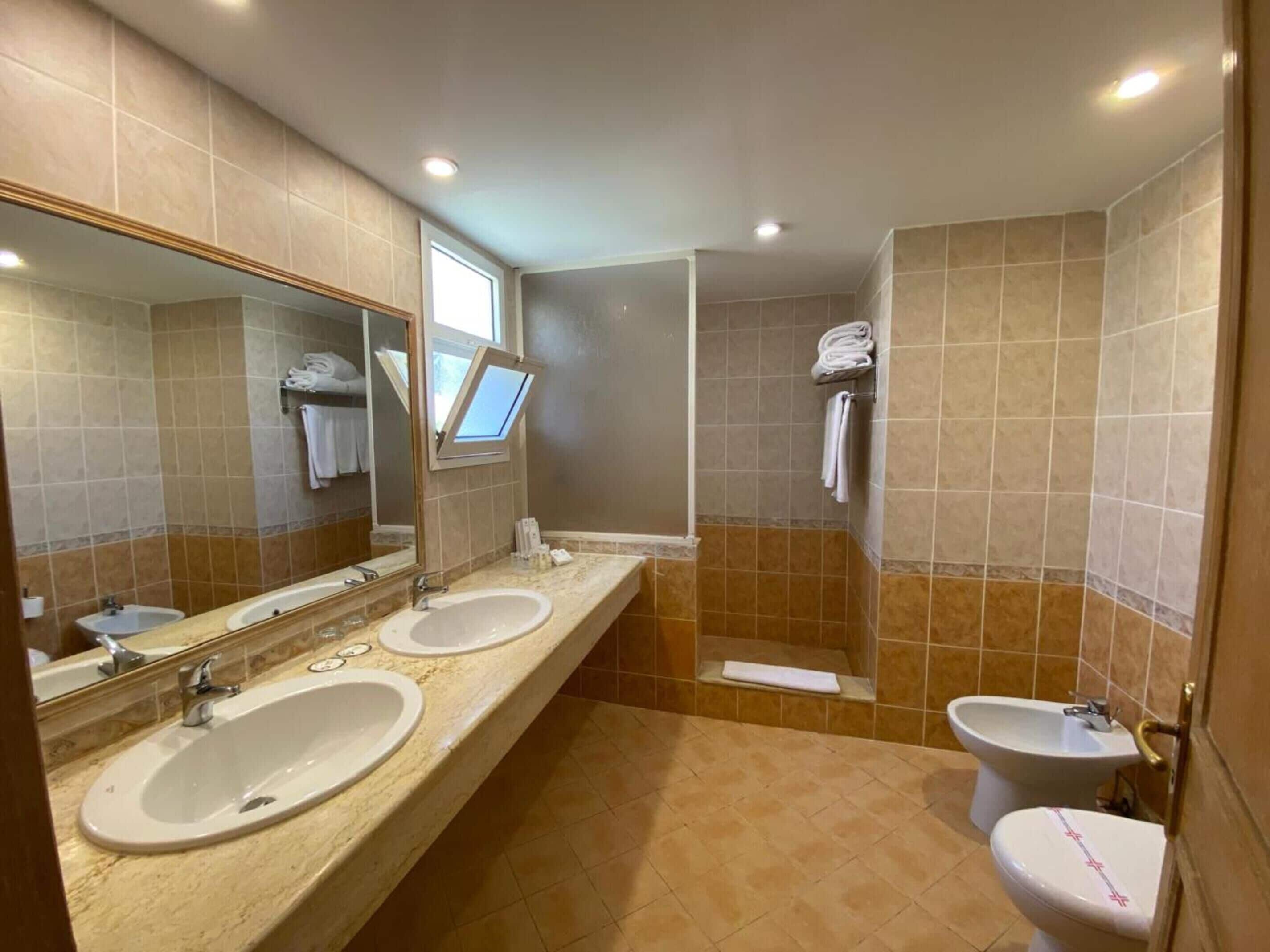 A bathroom with two sinks, a bidet, a shower, and a toilet.