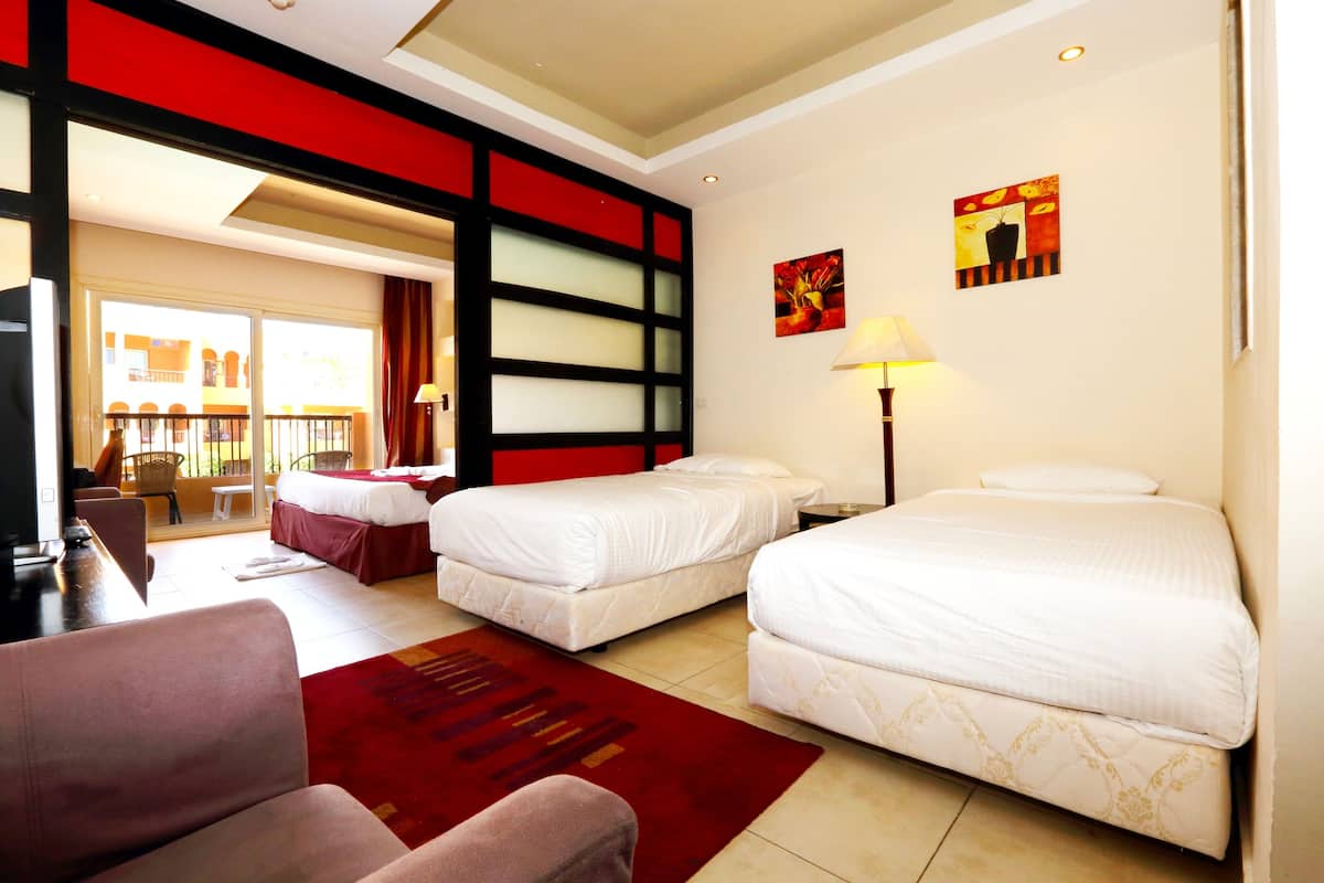 Une chambre d’hôtel avec deux lits, un mur d’accent rouge, un balcon avec vue et une moquette rouge.