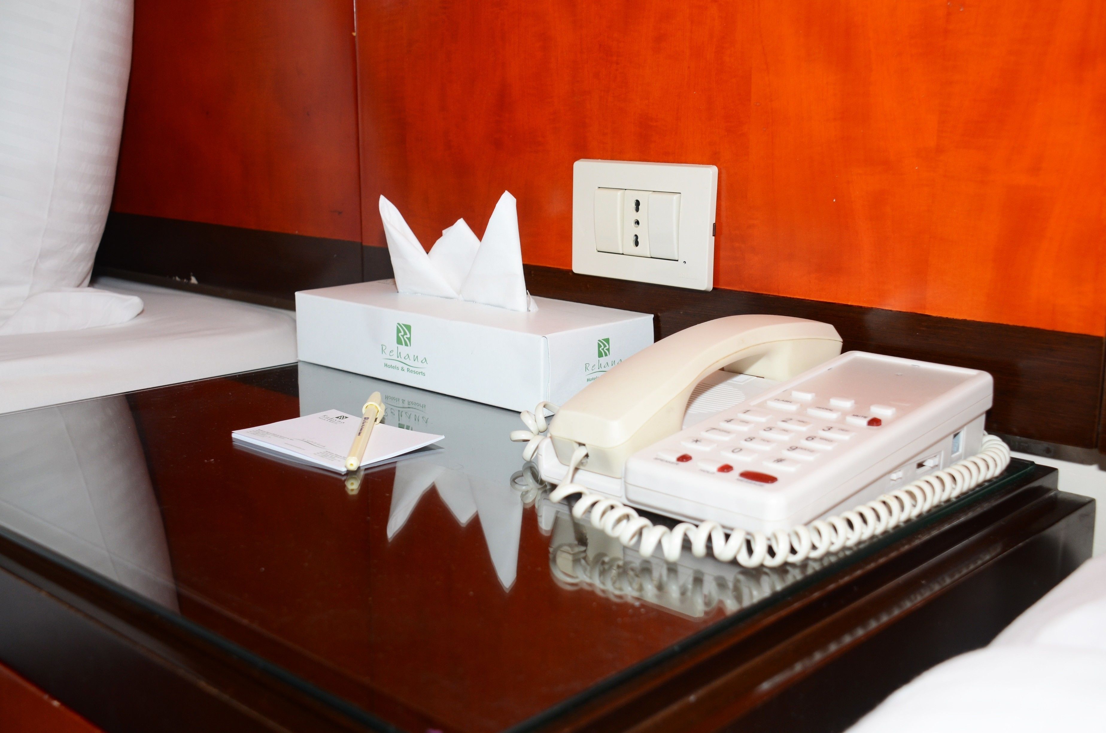 Una habitación de hotel con una mesita de noche que contiene una caja de pañuelos, un bloc de notas y un teléfono.