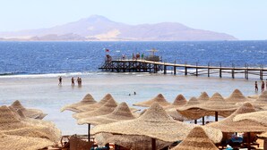 A beach with thatched umbrellas and a pier extending into the sea. - Rehana Royal Beach Resort - Aquapark & Spa - Families & Couples Only -  Premium Ultra All-Inclusive 24H (Sharm El Sheikh)