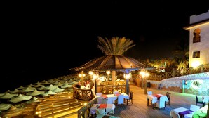 An outdoor dining area with wooden tables and chairs, surrounded by umbrellas and a wooden deck. - Rehana Royal Beach Resort - Aquapark & Spa - Families & Couples Only -  Premium Ultra All-Inclusive 24H (Sharm El Sheikh)