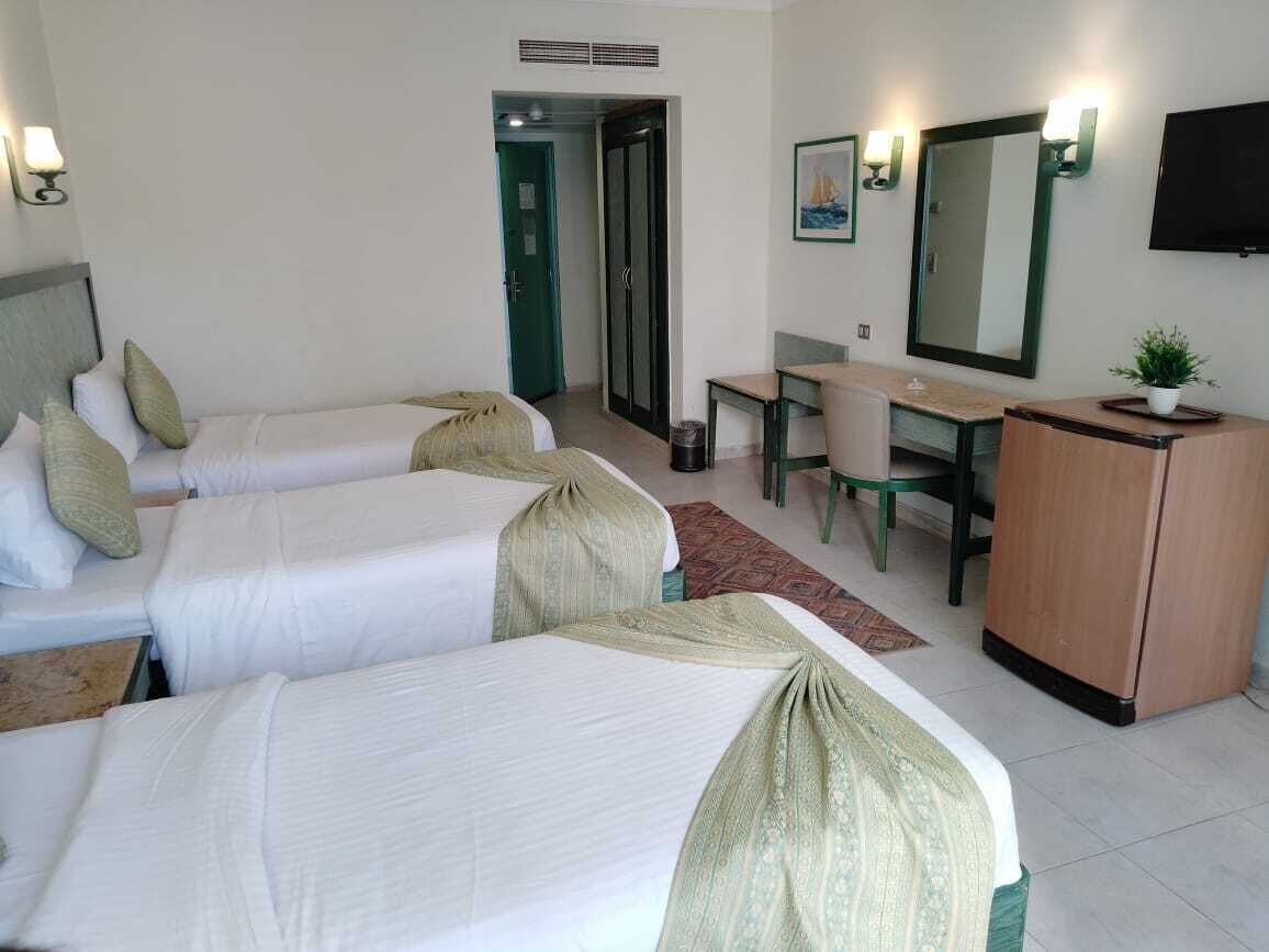 A hotel room with three single beds, a desk, a chair, a television, and a mirror.