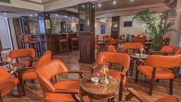 A restaurant with orange leather chairs, wooden tables, and a bar area with a mirror and wine bottles.