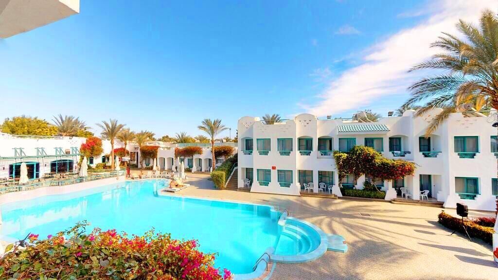 A hotel with a swimming pool, white buildings, and palm trees.