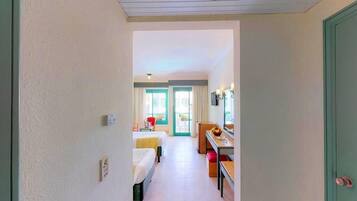 Een smalle gang die leidt naar een slaapkamer met een bed, een bureau en een stoel.
