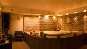 Un área de spa con una bañera grande, una estatua y un espacio de descanso con una silla y una pequeña mesa con bebidas.