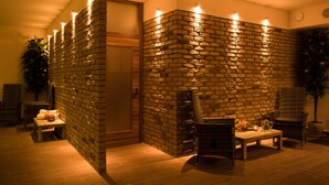 Una habitación con pared de ladrillo, puerta de madera, una pequeña mesa con una vela y dos sillas de mimbre.