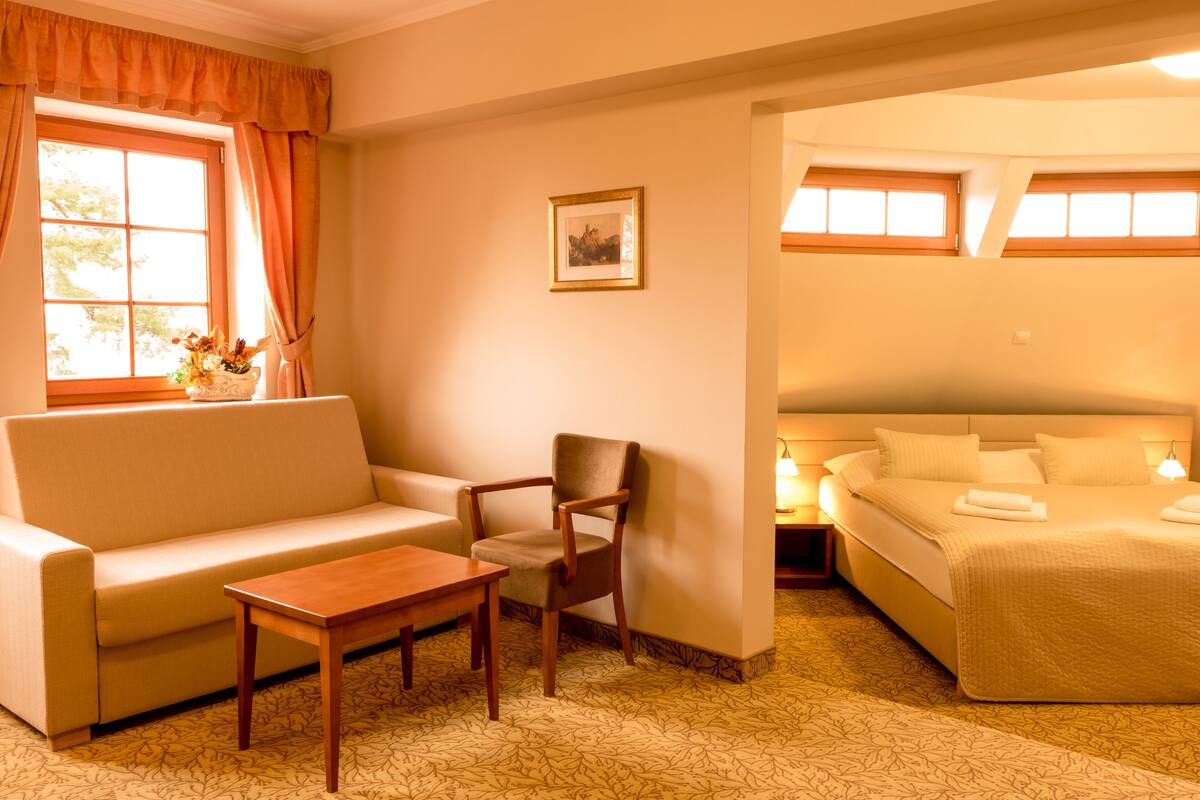 A hotel room with a sofa, a wooden chair, a small table, and a bed with a headboard.