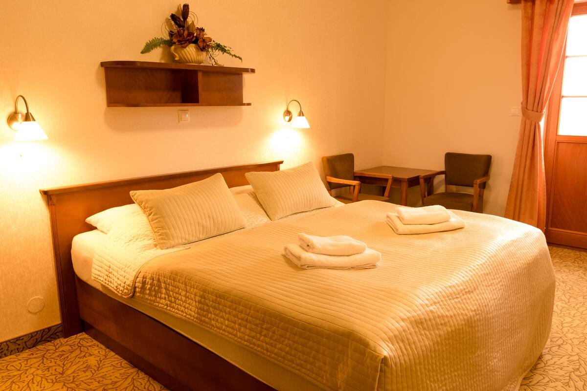 A hotel room with a large bed, two bedside lamps, a small table, and a chair.