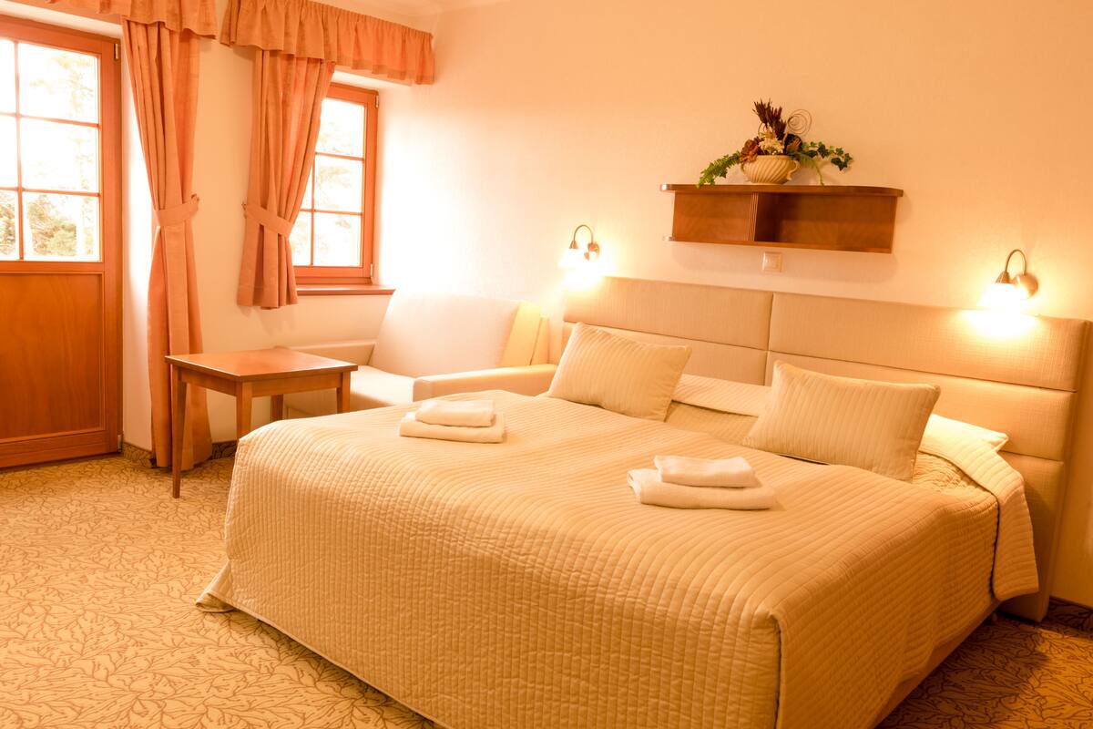 A hotel room with a large bed, a bedside table, a small desk, and a window with curtains.