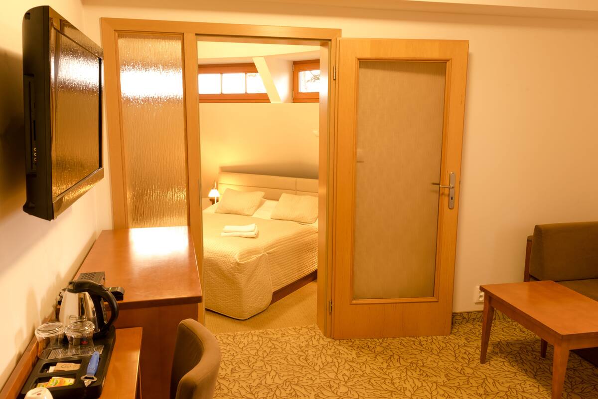 A hotel room with a bed, a desk with a kettle, a chair, and a sofa.
