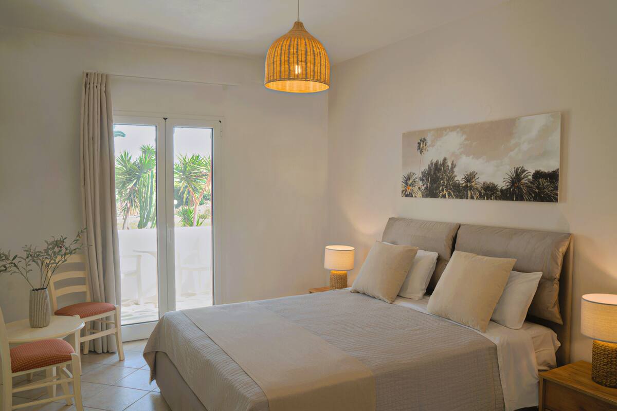 A bedroom with a bed, a chair, a table, a lamp, and a painting on the wall.