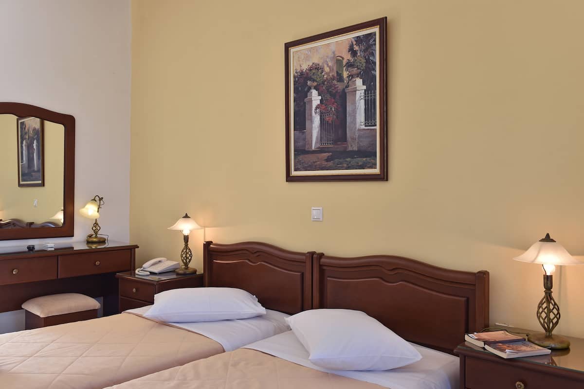 A hotel room with a double bed, bedside tables with lamps, a dresser, a mirror, and a framed painting on the wall.