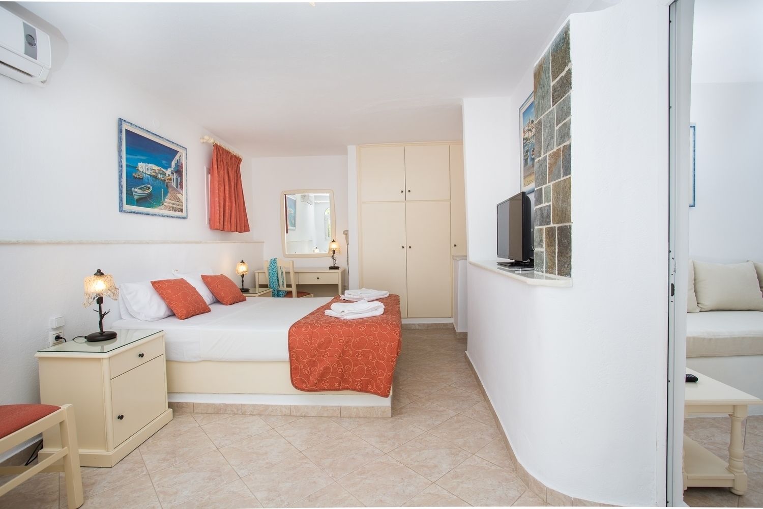 Habitación de hotel con cama, mesitas de noche, escritorio, televisión y baño visible a través de una puerta abierta.