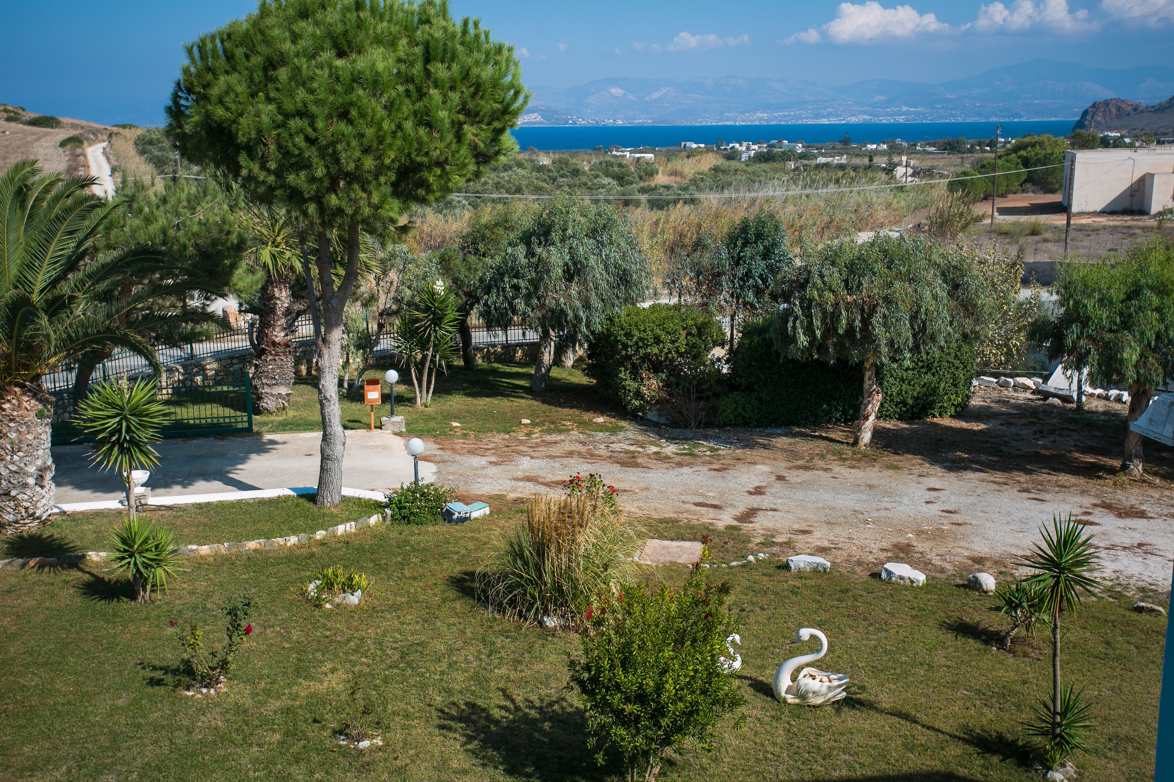 Un jardin aménagé avec une grande variété d’arbres et d’arbustes, une sculpture de cygne et une vue sur la mer et les montagnes lointaines.