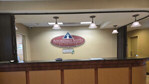 Un mostrador de recepción con un letrero que dice "Affordable Suites of America" y una placa que dice "Hogar, dulce hogar". Hay tres lámparas colgantes sobre el mostrador.