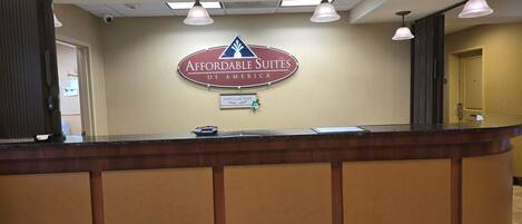 Un mostrador de recepción con un cartel de Affordable Suites of America, una cámara de seguridad y una puerta a la derecha.