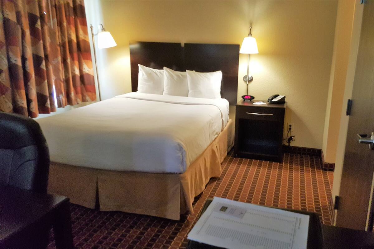 Una habitación de hotel con una cama, una mesita de noche, una silla y una puerta.