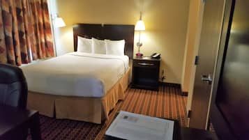 Una habitación de hotel con una cama, una mesita de noche, una silla y una puerta.