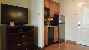 Una cocina compacta con armarios de madera, microondas integrado, refrigerador y lavavajillas. Un televisor de pantalla plana está montado en un mueble de madera.