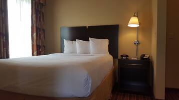 A hotel room with a large bed, a nightstand with a lamp, and a digital clock displaying the time.