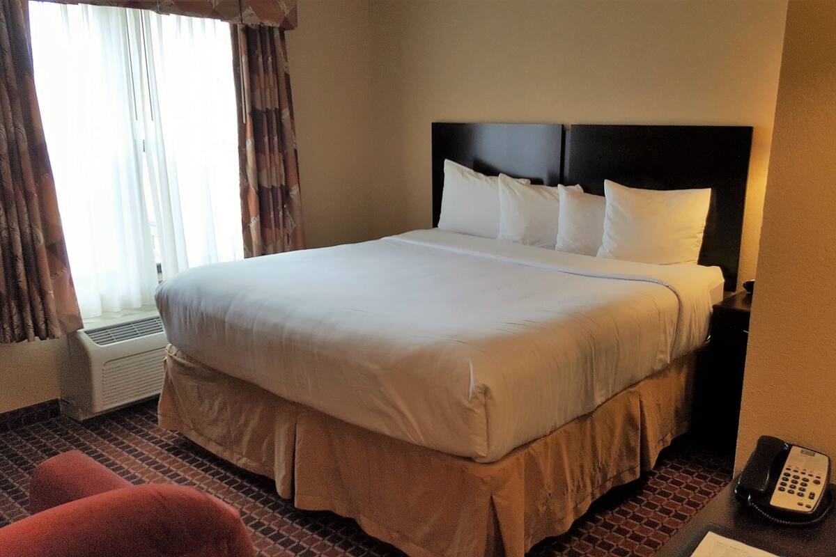 Habitación de hotel con una cama grande, un teléfono en la mesita de noche y una ventana con cortinas.