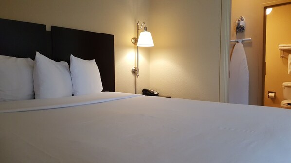 Una habitación de hotel con una cama grande, un teléfono en la mesita de noche y una lámpara de pared.