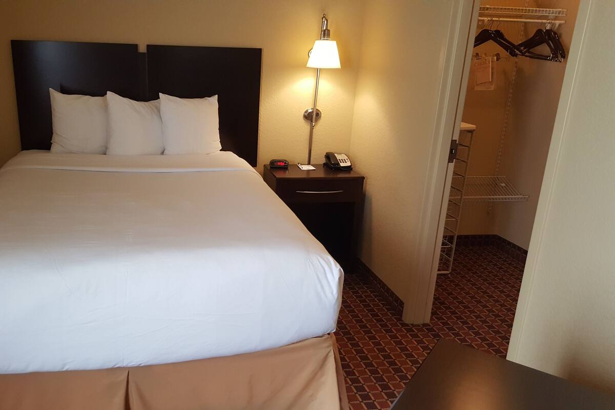 Una cama bien hecha con ropa blanca, una mesita de noche con una lámpara y otro con un teléfono.