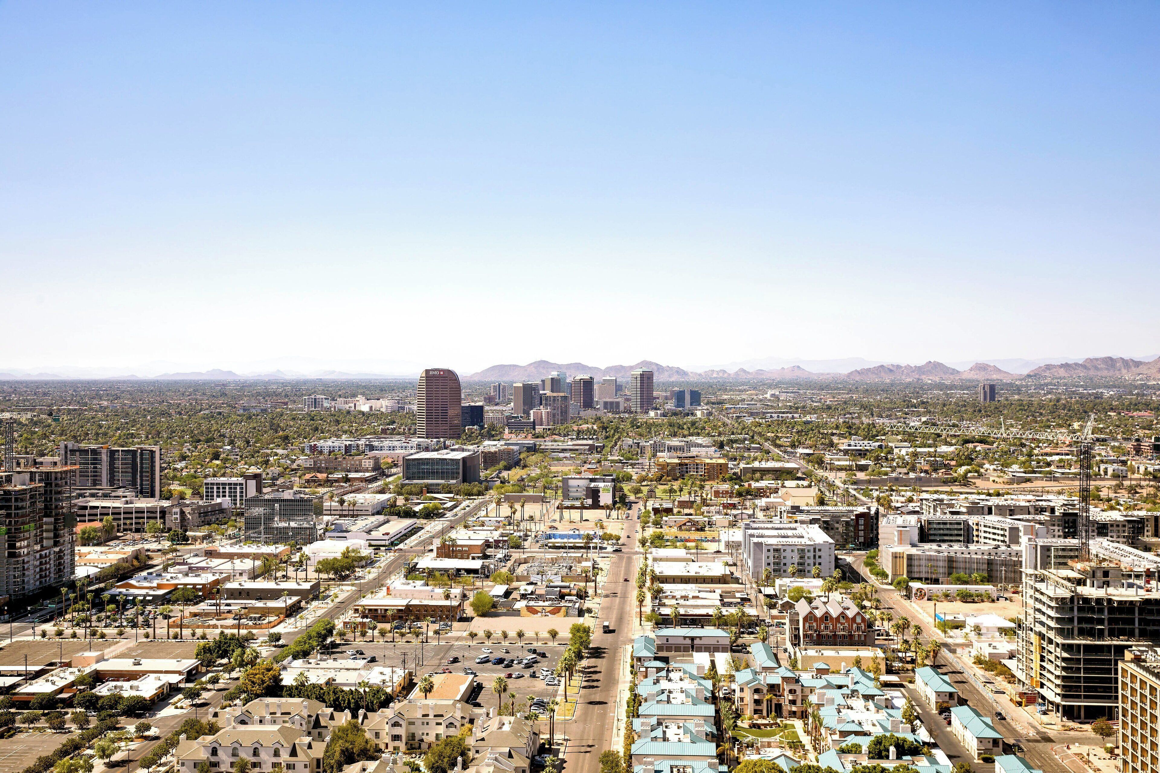 A cityscape with a mix of modern and older buildings, a clear sky, and distant mountains.