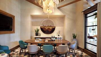 A dining area with a round table, chairs, a chandelier, a wall-mounted decorative piece, and potted plants.