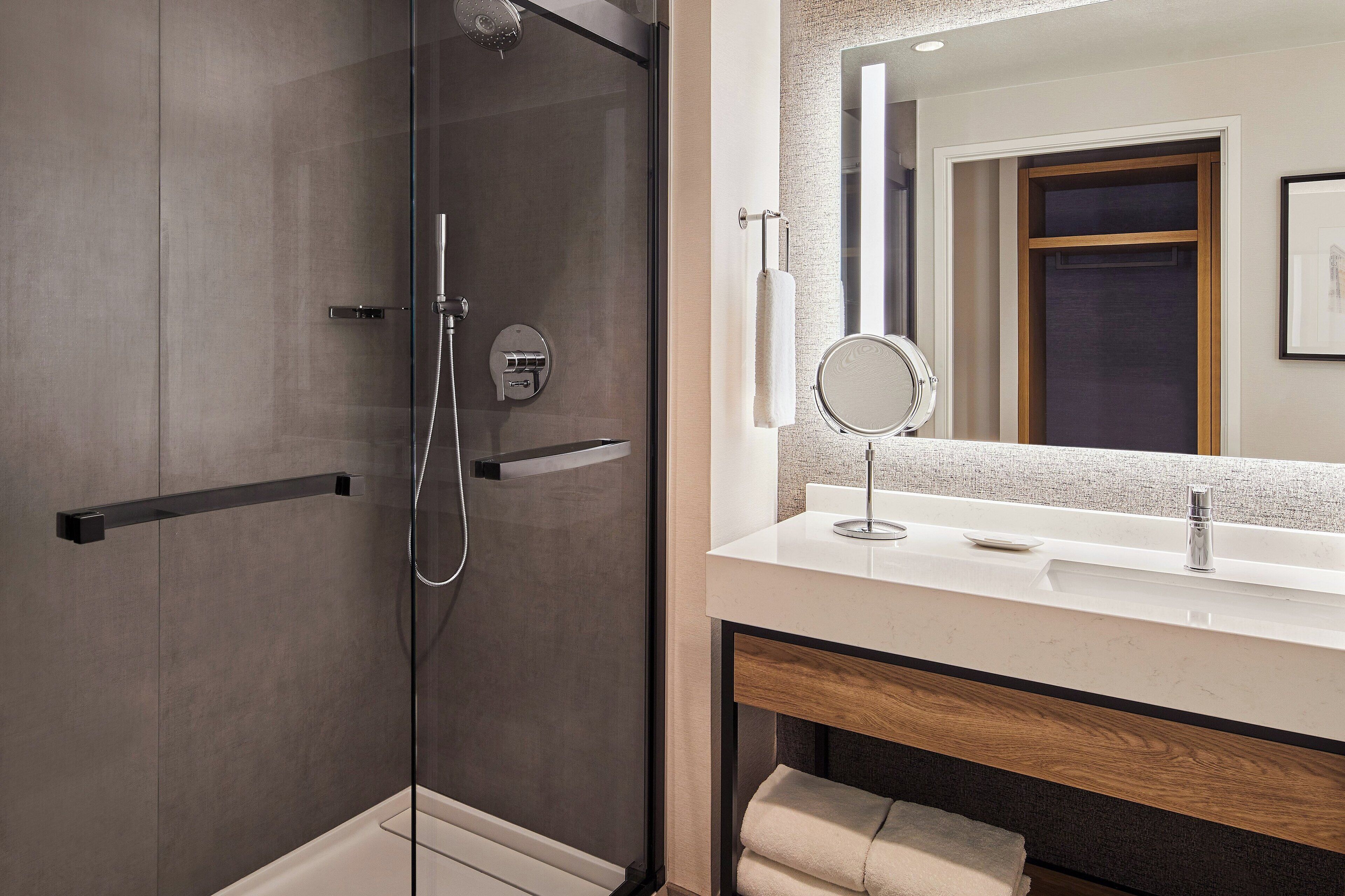A modern bathroom with a glass-enclosed shower, a large mirror, and a white countertop.