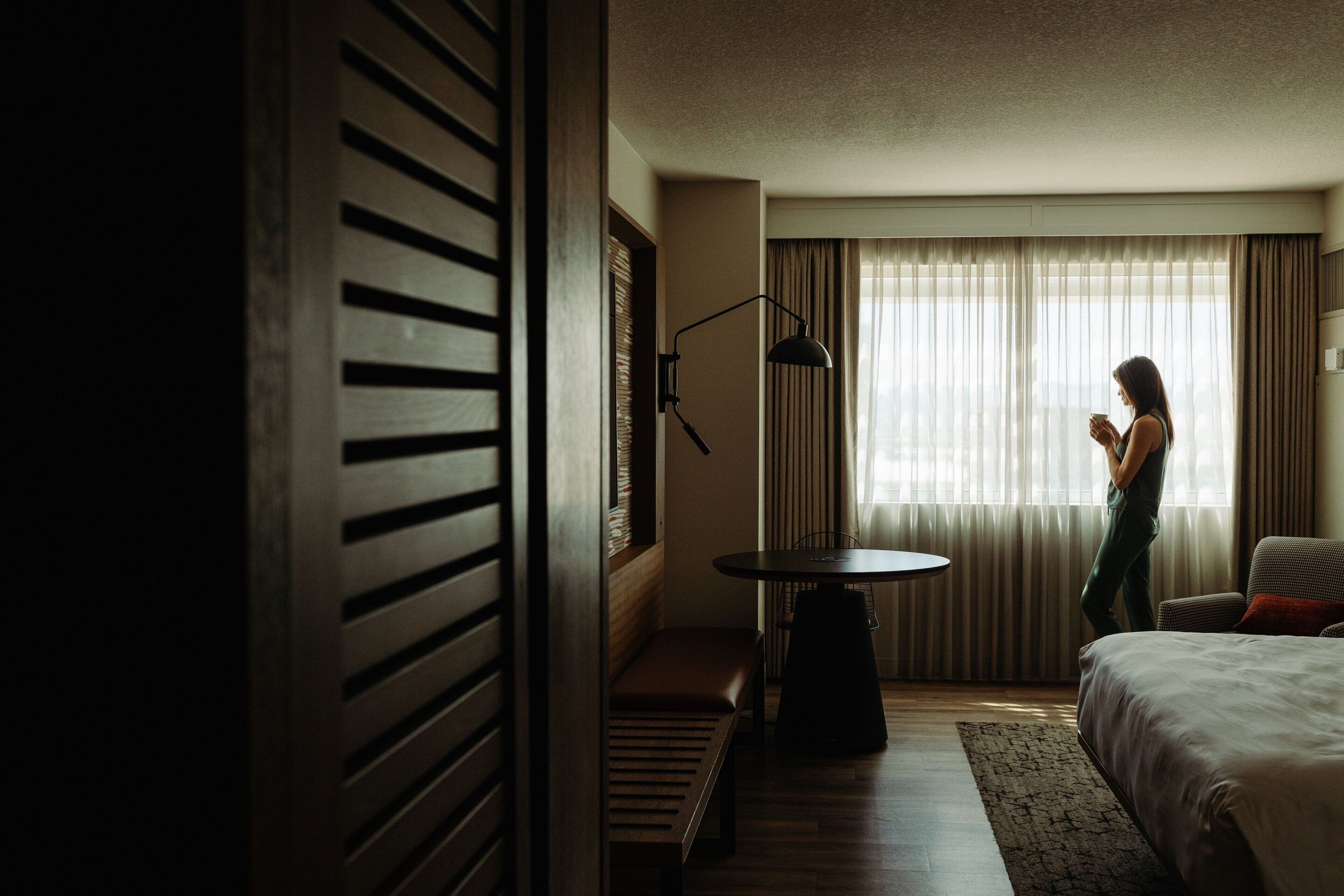 Una camera d'albergo con un letto, una scrivania, una sedia, una lampada e una finestra con tende.