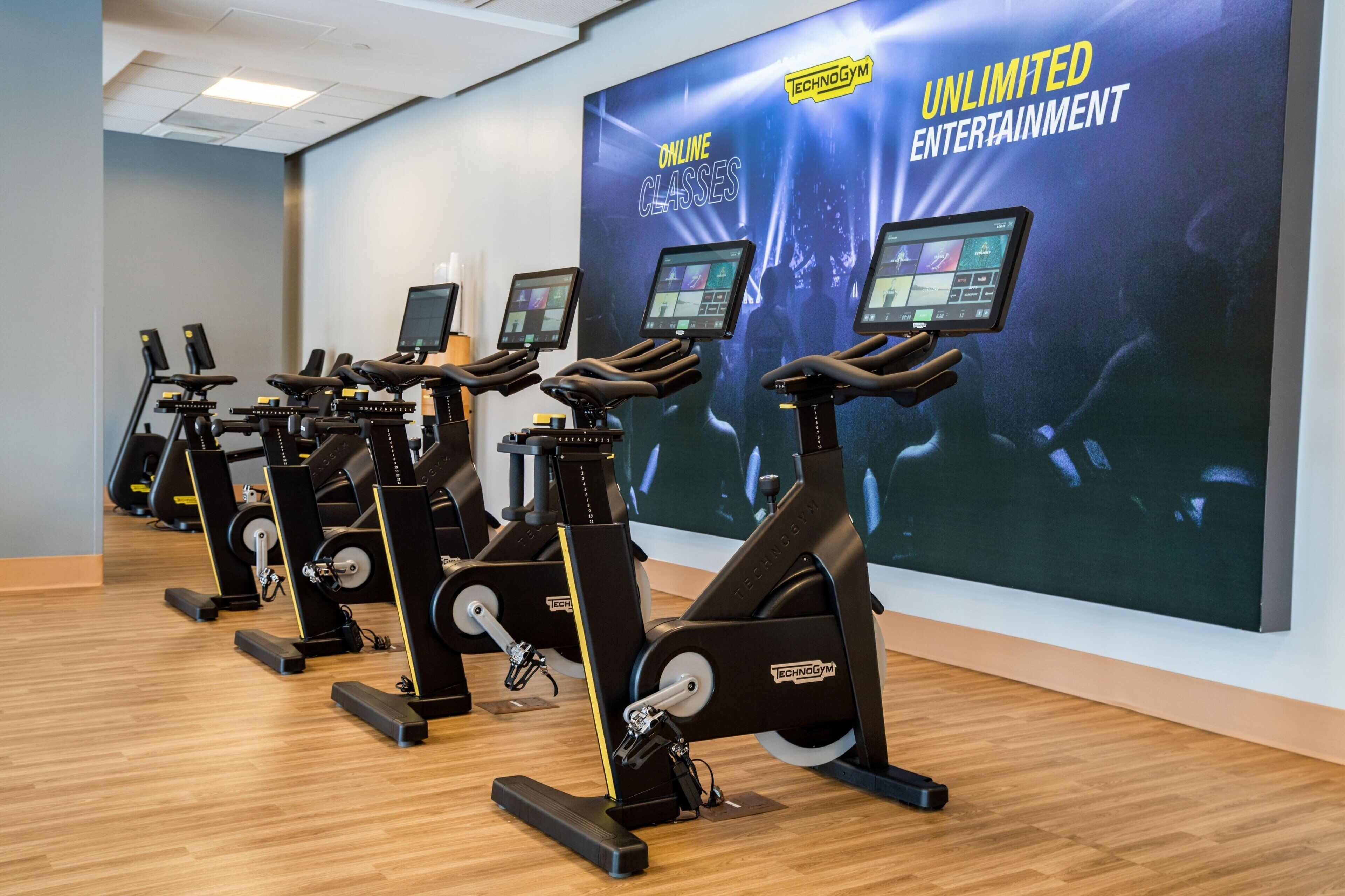 A row of stationary bikes in a gym with a large screen displaying 'Unlimited Entertainment'.