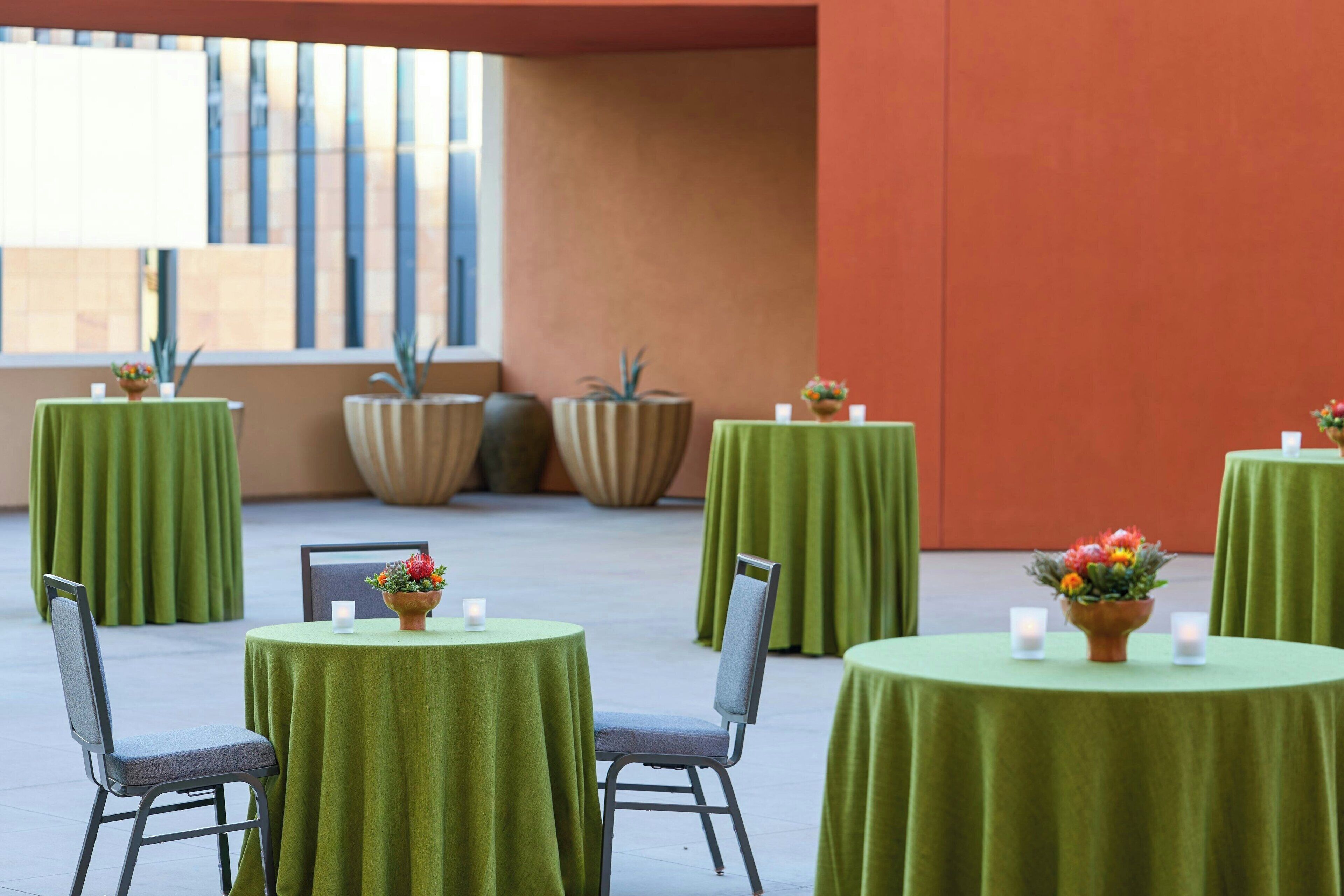 Un comedor con mesas redondas cubiertas con manteles verdes, sillas y plantas en macetas.